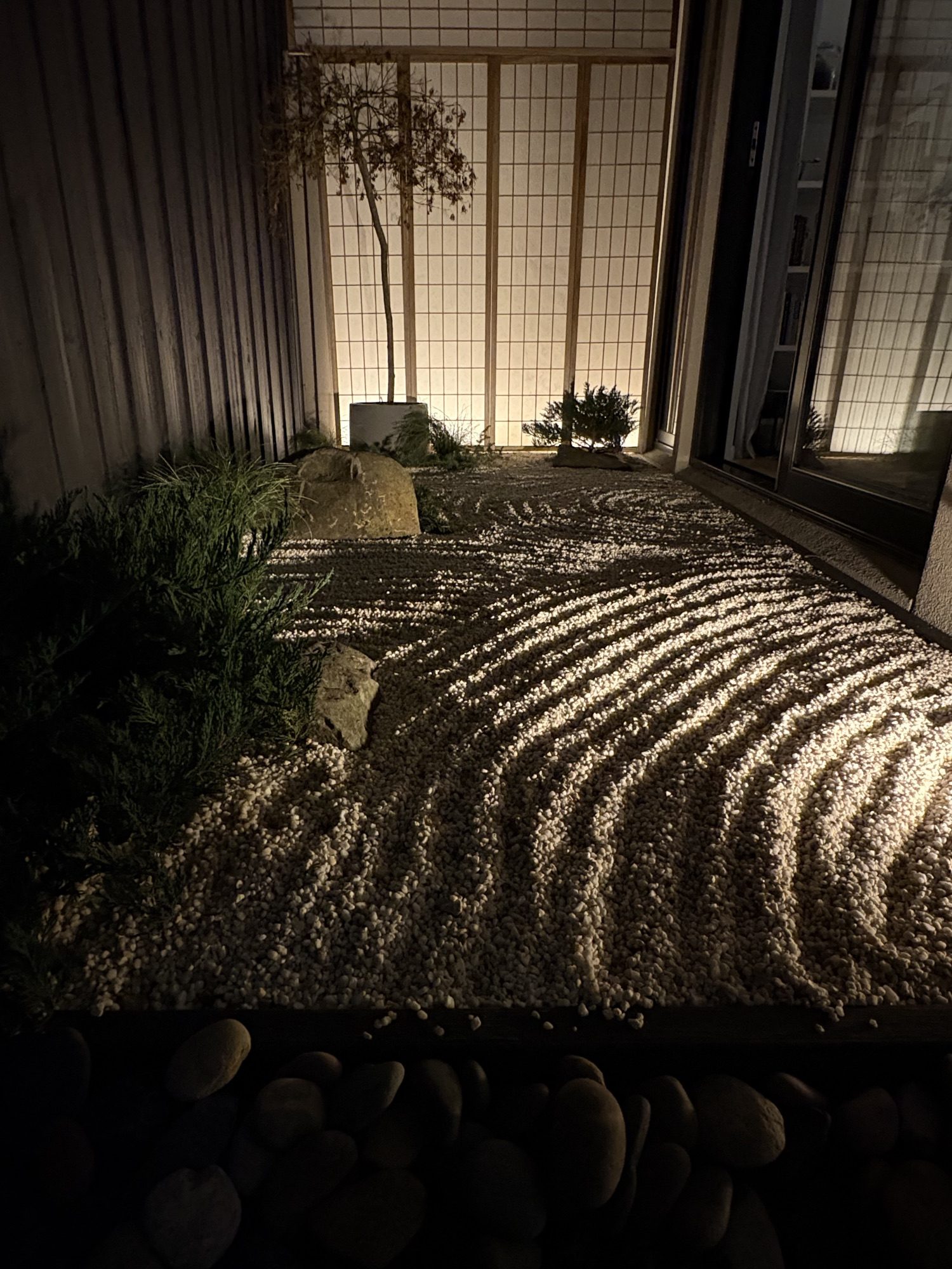 The finished garden lit at night, raked lines catching the light